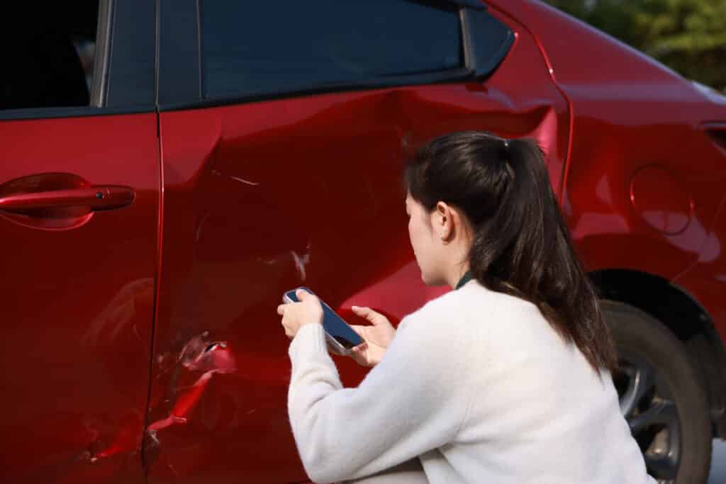 A woman taking a photo of the side swipe damage on her car.